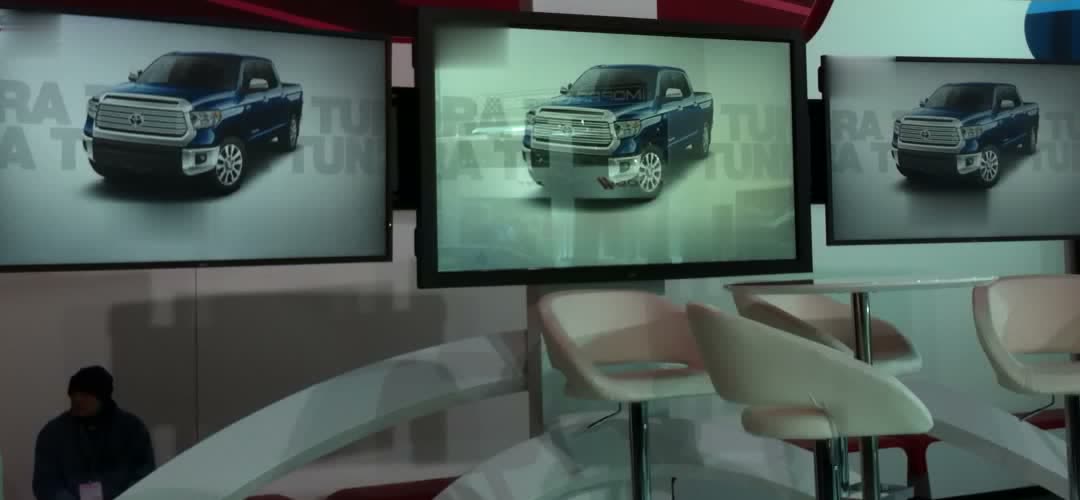 Three synced screens behind an auto show presenter stage